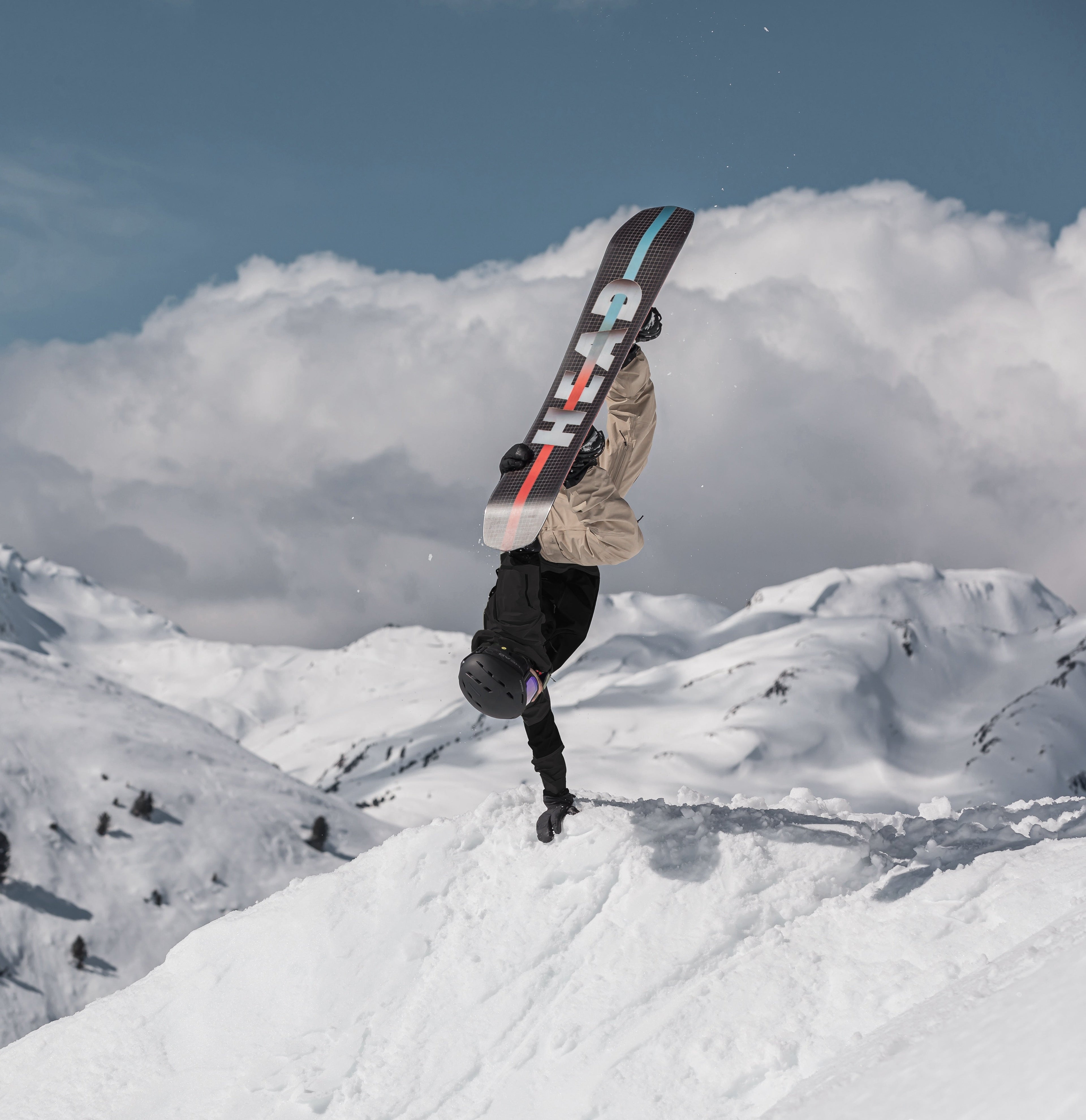 Snowboardzista wykonujący trick na desce snowboardowej w górskim, zaśnieżonym terenie